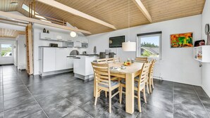 Una cocina moderna con armarios blancos, un comedor con mesa y sillas de madera, y un ventanal que ofrece vistas al exterior.