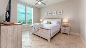 A bedroom with a bed, bedside tables, a ceiling fan, and artwork on the wall. - Sapphire 505 - By GISO Vacation Rentals (South Padre Island)