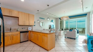 A modern kitchen with wooden cabinets, a central island, and a dining area with a white sofa and a balcony with a view. - Sapphire 505 - By GISO Vacation Rentals (South Padre Island)