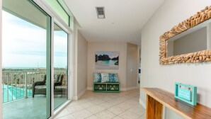 A spacious balcony with a view of the beach and ocean, a seating area with a bench and cushions, and a wooden console table with a framed picture. - Sapphire 505 - By GISO Vacation Rentals (South Padre Island)