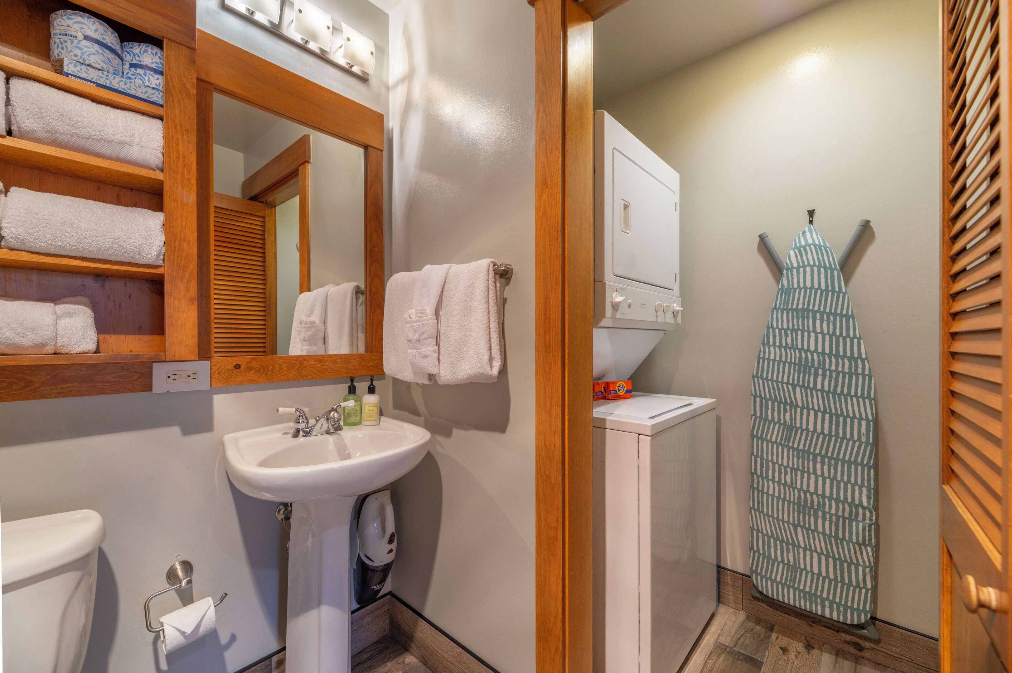 A bathroom with a wooden shelf holding towels, a sink with a mirror, and a towel rack.