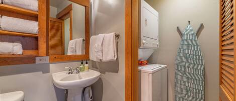 A bathroom with a wooden shelf holding towels, a sink with a mirror, and a towel rack.