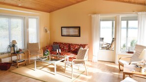 Un salón amplio con techo de madera, un sofá rojo estampado, una mesa de centro de cristal y vistas al exterior a través de amplias ventanas.