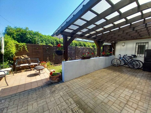 An outdoor patio area with a pergola, seating, potted plants, and bicycles.