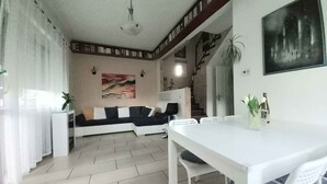 A modern living room with a sofa, a dining table with chairs, a staircase, and a painting on the wall. - Ferienhaus mit Pool und Internet (Balatonmáriafürdő)