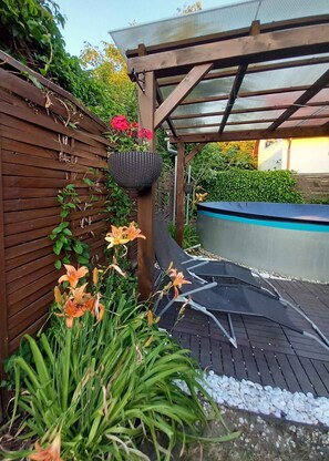 A wooden deck with a pergola, a hanging basket, and a variety of plants including lilies. - Ferienhaus mit Pool und Internet (Balatonmáriafürdő)