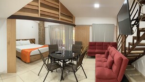 Una camera d'albergo compatta con angolo cottura, un letto con coperta arancione, un'area pranzo con tavolo e sedie e un divano rosso.
