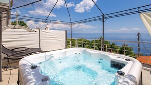 Un bain à remous sur un balcon offrant une vue dégagée sur la mer et les montagnes.