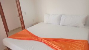 En säng med vita sängkläder och en orange filt.