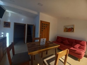 A dining area with a wooden table and chairs, a red sofa, and a staircase leading to another room.