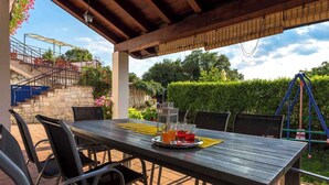 An outdoor patio with a wooden table set for two, surrounded by chairs. - Holiday home with outdoor pool (Kujići)