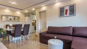 A modern living room with a brown sofa, a dining area with a table and chairs, a kitchen in the background, and a framed picture on the wall. - Holiday home with outdoor pool (Kujići)