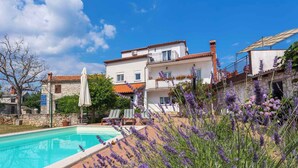 A pool area with lounge chairs, a white umbrella, and lavender plants. - Holiday home with outdoor pool (Kujići)