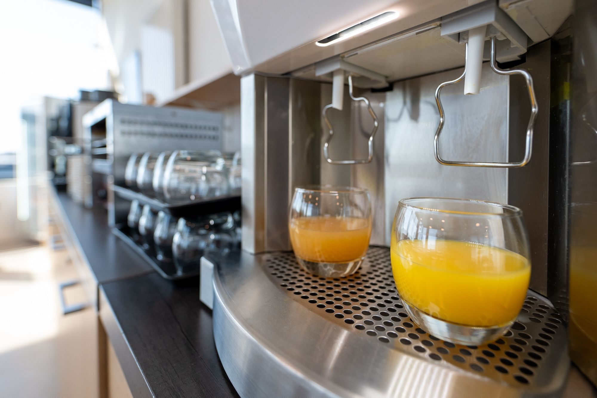 A coffee machine dispensing orange juice into two glasses.