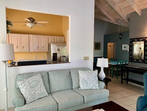 Ein Wohnzimmer mit einer Couch, einem Couchtisch, einem Essbereich mit Tisch und Stühlen, einer Küche mit Schränken und Geräten sowie einem Deckenventilator.
