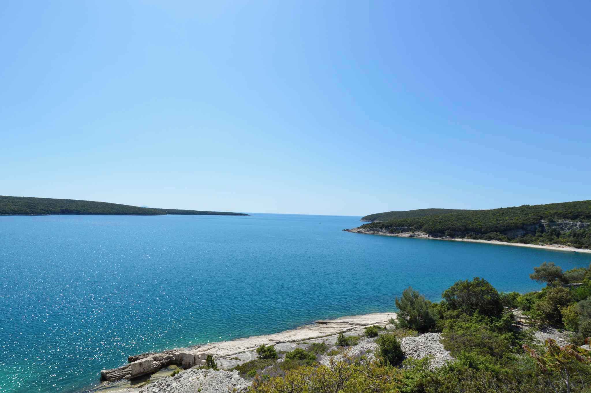 Eine Küstenlandschaft mit klarem, blauem Meer, felsiger Küste und grünen Hügeln.