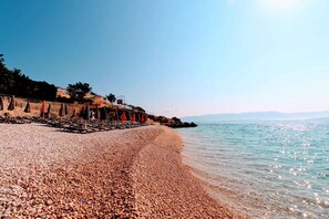Una spiaggia di ciottoli con un muro di pietra e ombrelloni.