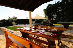 An outdoor dining area with a table set for two, a pool, and a covered seating area.