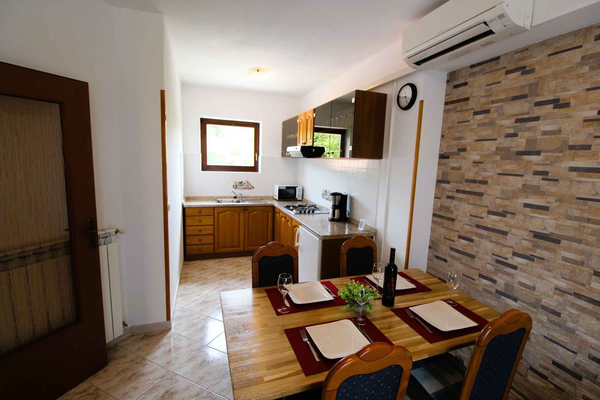 A dining area with a wooden table set for four, a kitchen in the background, and a clock on the wall.