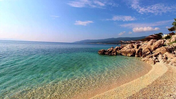 A clear coastal view with a pebble beach and rocky outcrops.