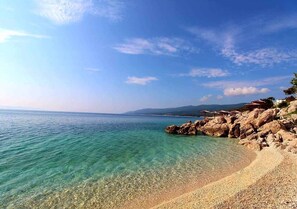 A clear coastal view with a pebble beach and rocky outcrops.