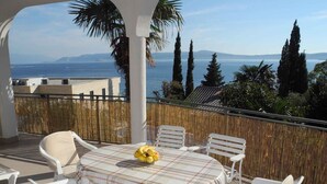 Una terraza con una mesa preparada para seis, sillas blancas y vistas al mar y a las montañas.