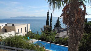 Una piscina con vista al mar, rodeada de palmeras y un edificio con techo de tejas.