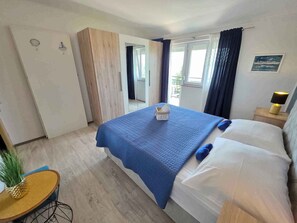 Ein Hotelzimmer mit Bett, einem kleinen Tisch mit einer Ananas, einem Nachttisch mit Lampe und Blick ins Freie.
