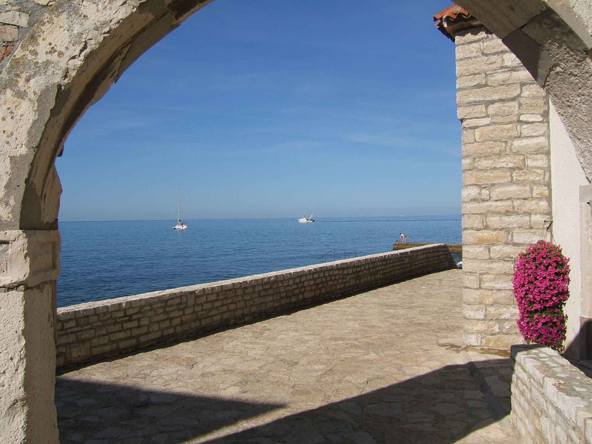 A stone archway overlooking a calm sea with boats.