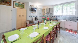 A modern kitchen with a dining area set for six. It includes a large island, a built-in oven, and a window providing natural light.