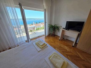 Een hotelkamer met een bed, een televisie, een kamerplant en uitzicht op zee.
