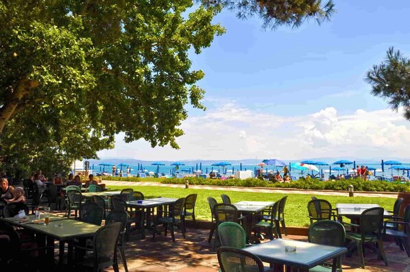 An outdoor dining area with tables and chairs, a view of the beach, and umbrellas.