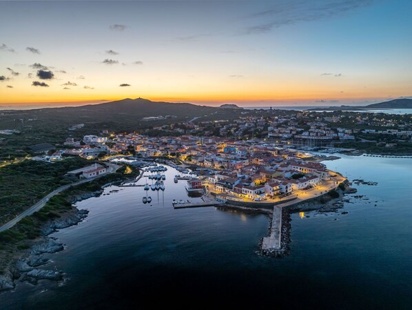 An aerial view of a coastal town at dusk with a marina, houses, and a prominent building with a red roof. - Beautiful apartment for 4 guests with WIFI, A/C, pool, TV, terrace and pets allowed (Stintino)