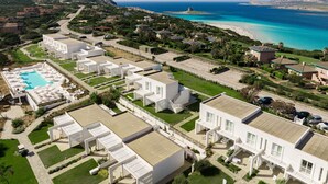 Zona residencial costera con edificios blancos modernos, una piscina y una playa al fondo.