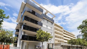 Un edificio de varios pisos con balcones, césped verde y automóviles estacionados.