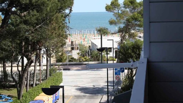 Blick auf einen Strand, im Vordergrund eine Straße und ein Gebäude mit einem Balkon.