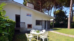 A white building with a patio area, a table with chairs, and a sign on the wall. - Holiday home mit Garten (Lignano)