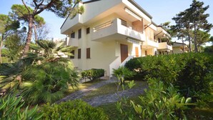 A two-story building with a balcony on the upper floor, surrounded by lush greenery and trees. - Studio with balcony for 3 people (Lignano)