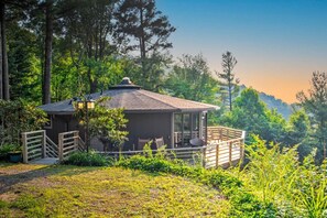 A small, single-story cabin with a porch and a covered outdoor seating area, surrounded by lush greenery and trees. - Amazing Town Mountain Getaway (Asheville)