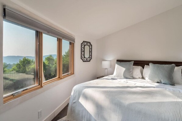 A bedroom with a large window, a bed with white bedding, and a wall-mounted mirror. - Amazing Town Mountain Getaway (Asheville)