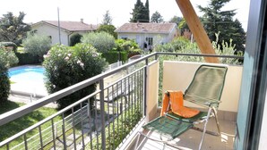 A balcony with a metal railing, a green chair, and a view of a swimming pool and houses in the background.