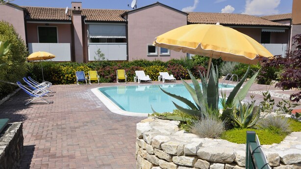 A pool area with a stone wall, a pool, and several chairs and umbrellas.