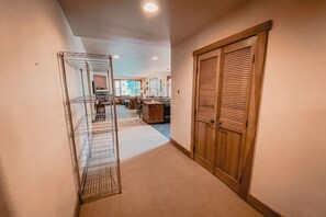 A hallway with a metal shelving unit, a wooden door, and a kitchen area in the background. - Red Hawk Townhomes 2321 (Keystone)