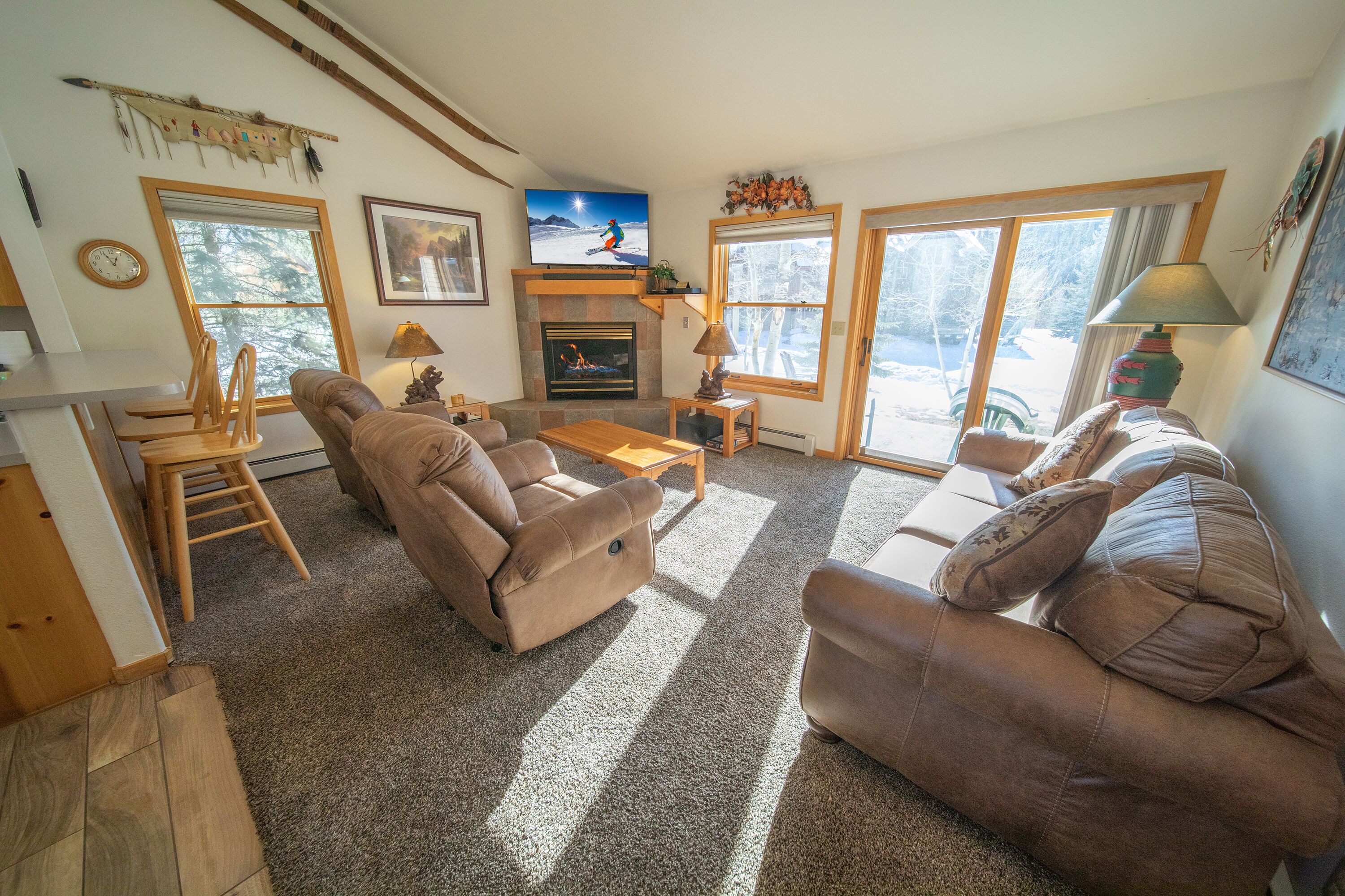 A cozy living room with a fireplace, comfortable seating, and large windows offering a view of the outdoors.