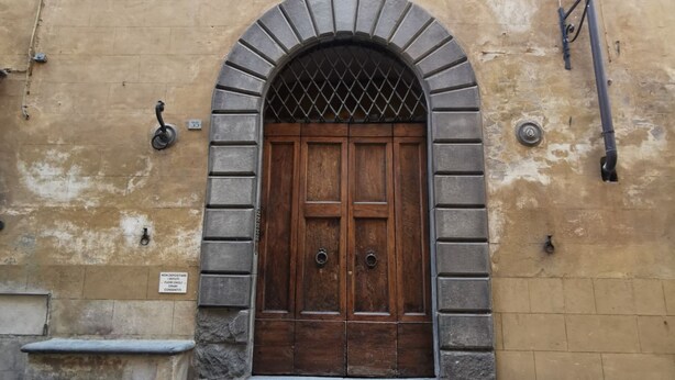 A wooden double door with a metal grille, set within a stone archway. - BANDINI 35-central with elevator and air conditioning (Siena)