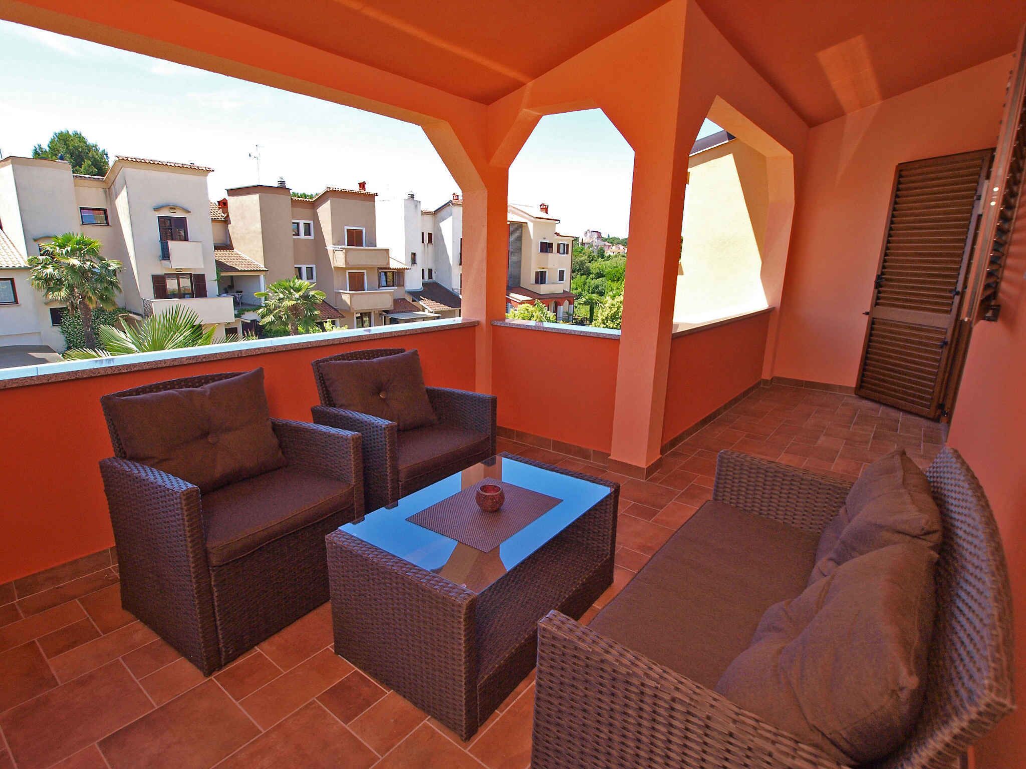 A balcony with wicker furniture, a glass-top table, and a view of neighboring buildings.