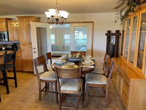 A dining area with a round table set for four, surrounded by wooden chairs. A chandelier hangs from the ceiling, and a wooden cabinet with glass doors is to the right.