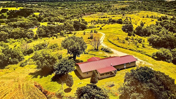 A rural landscape with a single house featuring a red roof, surrounded by lush greenery and a winding path.