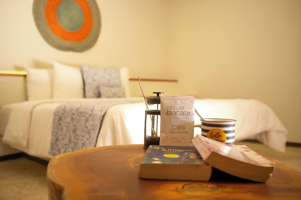 Ein Hotelzimmer mit einem Bett, einer Kaffeemaschine, einer Tasse und einem Buch auf einem Holztisch.