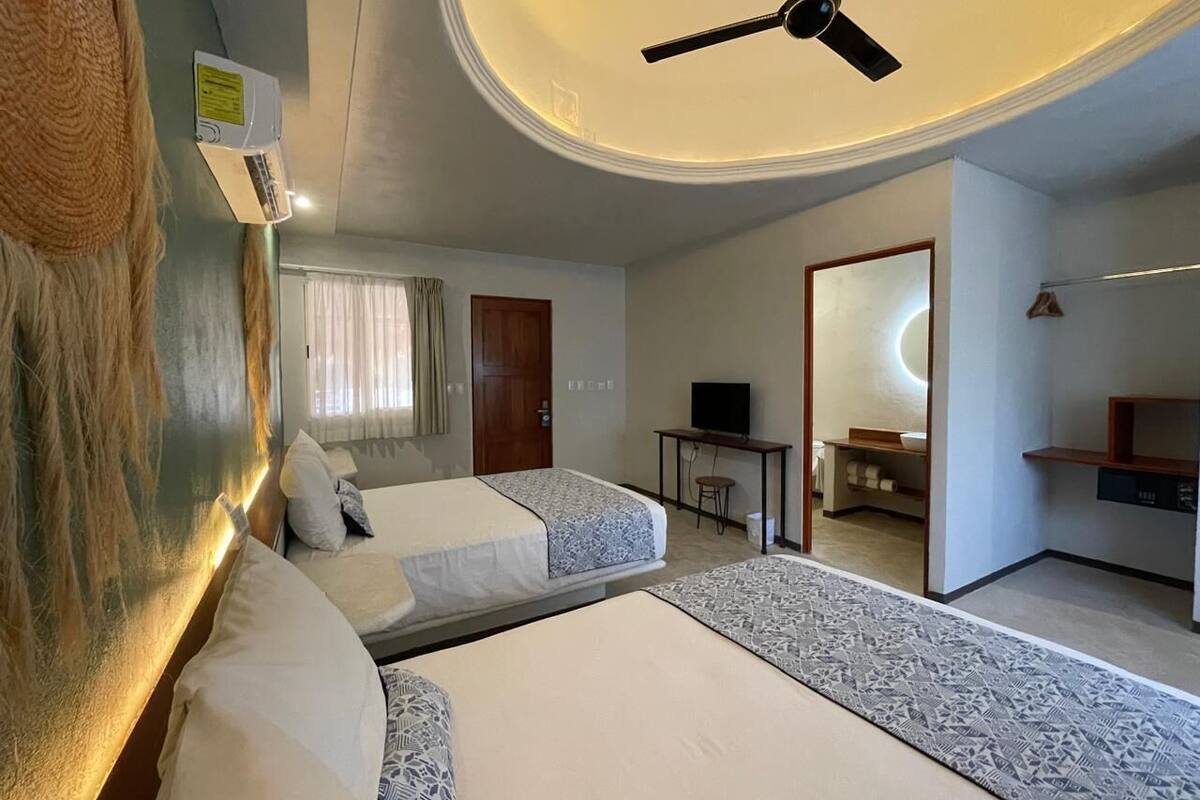 Ein Hotelzimmer mit zwei Betten, einem Deckenventilator, einem Fernseher, einem kleinen Tisch und einem durchgegangenen Tür zu einem Badezimmer.